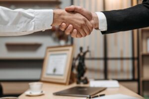 Legal Transcription 1 https://cleglex.com/legal-transcription/ Close-up of a handshake between two professionals in a modern office setting, emphasizing partnership and agreement.