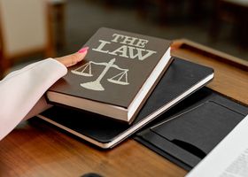 Closeup image of a law book titled 'The Law' on a wooden desk with scales of justice.